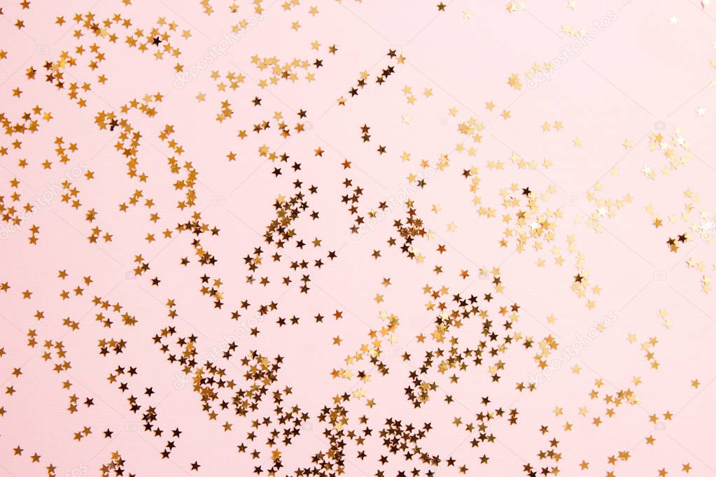 Golden star sprinkles on pink background. Festive holiday background. Celebration concept. Top view, flat lay.