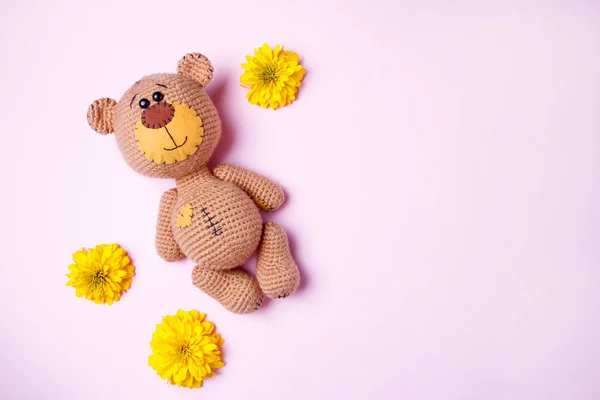 Amigurumi oso de peluche hecho a mano con crisantemo amarillo aislado sobre un fondo rosa. Fondo de bebé. Copiar espacio, vista superior . — Foto de Stock