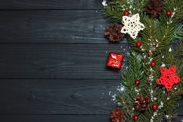 Las ramas verdes del árbol de Navidad con el pino y los juguetes sobre el fondo negro de madera. Copiar espacio, plano laico . —  Fotos de Stock