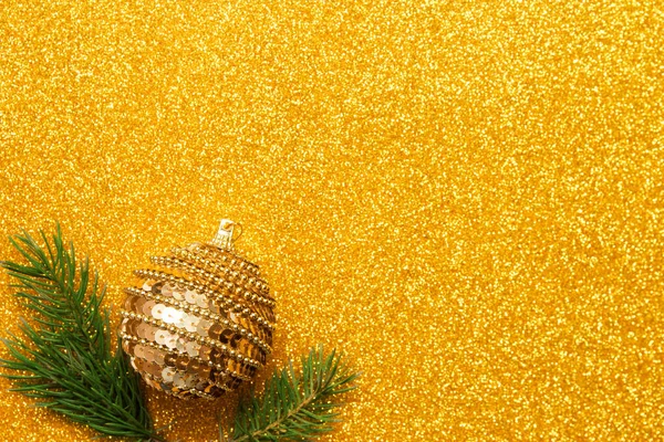 Dekorativní míč s vánoční strom větve na zlatém třpytivém pozadí. Minimalistický koncept — Stock fotografie