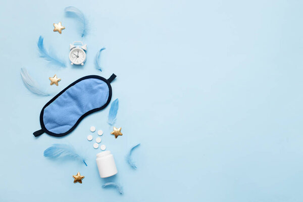 Pills, bottle, sleeping mask and white alarm clock with stars on blue pastel background. Concept Insomnia, sleep problems, time to take pills and treatment. Top view, flat lay, copy space