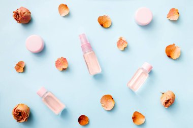 Çiçeklerin ve kozmetik ürünlerinin düzlüğü, Rose 'un esaslı yağı: toner, serum, özü, nemlendirici ve mavi arka plandaki diğerleri, üst görünüm, afiş. Yüz bakımı güzelliği