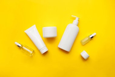 Parlak sarı arka planda kozmetik şişeleri, üst manzara, kopyalama alanı. Model yap. Beyaz kavanozlar, banyo aksesuarları. Yüz ve vücut bakımı kavramı.
