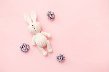 Pembe arka planda çiçekli örülmüş tavşan amigurumisi. Bebek geçmişi. Boşluğu kopyala, üst görünüm.
