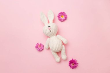 Pembe arka planda izole edilmiş çiçek kasımpatı ile örülmüş tavşan amigurumisi. Bebek geçmişi. Boşluğu kopyala, üst görünüm.