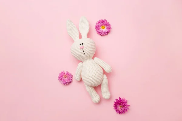 Pembe arka planda izole edilmiş çiçek kasımpatı ile örülmüş tavşan amigurumisi. Bebek geçmişi. Boşluğu kopyala, üst görünüm.