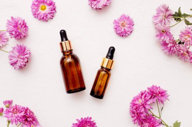 Damlatan cam şişelerden oluşan düz bir döşeme. Cilt, çiçek kasımpatıları eşliğinde beyaz arka planda asgari düzeyde taklit edilebilecek temel yağ ürünleri.