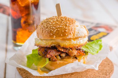 Beyaz arka plan üzerinde kızarmış yumurta burger Close-up. Kola ve gazete arka planda.