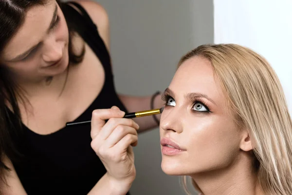 makeup stylist applying makeup on the model closeup beauty face