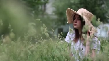 Yazın yeşil çimlerin üzerinde hasır şapkalı güzel beyaz kız. Seçili odak. Bulanık arkaplan. Bokeh.