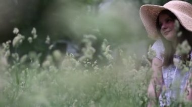 Yazın yeşil çimlerin üzerinde hasır şapkalı güzel beyaz kız. Seçili odak. Bulanık arkaplan. Bokeh.
