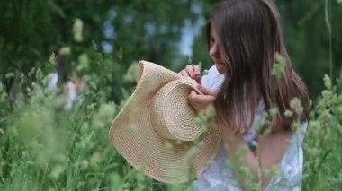 Kız hasır şapkasını küçük çayır çiçekleriyle süslüyor. Yazın dışarıda, yeşil çimlerin üzerinde. Seçili odak. Bulanık arkaplan. Bokeh.