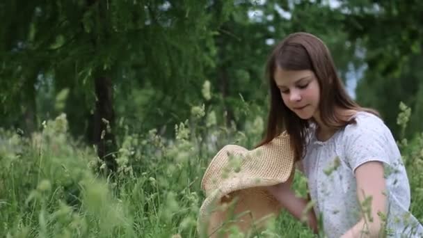 女の子は小さな牧草地の花で彼女のわらの帽子を飾る 夏に緑の草の中に外 選択したフォーカス 背景をぼかす ぼっけ — ストック動画