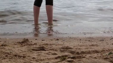 Deniz dalgalarında genç bacaklar ve yaz günü bulutlarda altın kum..