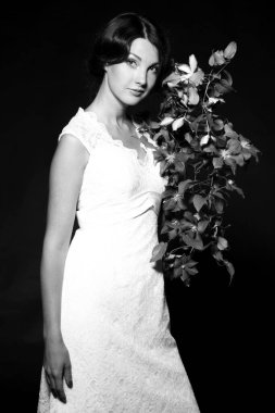 Siyah ve beyaz, siyah arka planda uzun beyaz elbiseli, gülümseyen genç bir kadının görüntüsü.