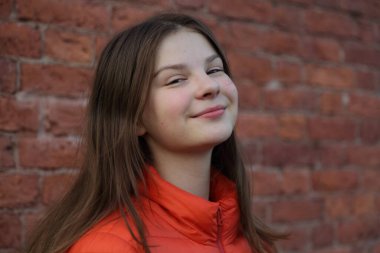 Güzel kız sonbaharda kırmızı tuğla duvarın üzerinde poz veriyor..