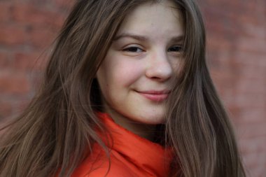 Güzel kız sonbaharda kırmızı tuğla duvarın üzerinde poz veriyor..