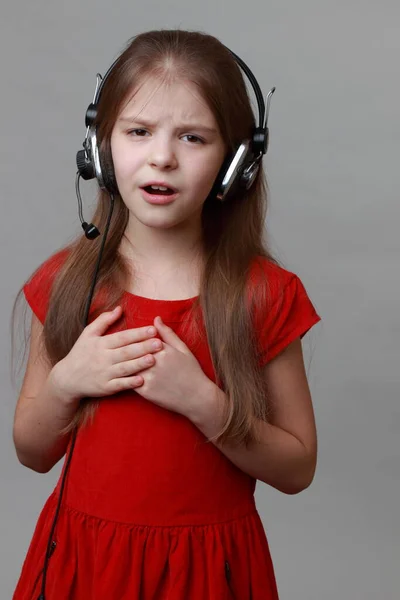 穿着漂亮红色衣服的小女孩拿着耳机和话筒唱歌 图库图片