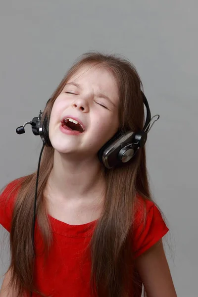 穿着漂亮红色衣服的小女孩拿着耳机和话筒唱歌 免版税图库照片