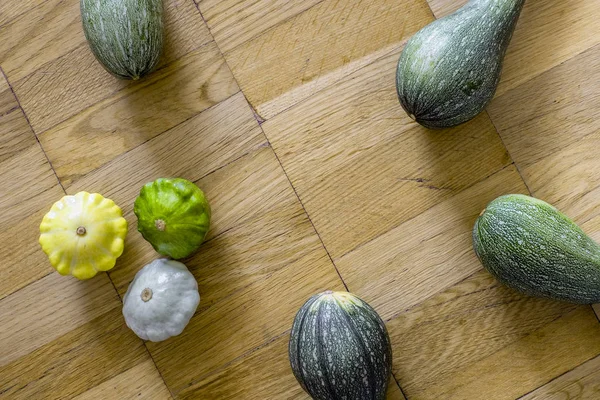 Four green zucchini with small scallop squashes over the light brown wooden background