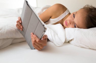 Güzel genç bayan haber, e-postaları, cevap okumak onun yatakta bir tablet bilgisayar ile bu o artık öyle tahmin hava kontrol ne bugün giymek