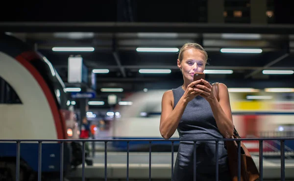 現代の駅で毎日の電車を待っている若い女性通勤者が 待っている間に携帯電話を使用しています カラートーン画像 — ストック写真