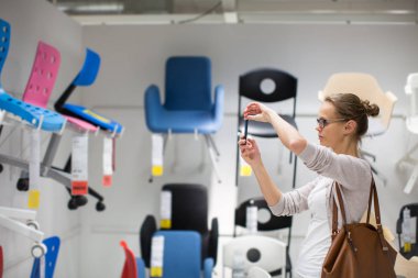 Güzel, genç bir kadın modern bir ev mobilyası mağazasında dairesi için doğru mobilyayı seçiyor (renk tonlu görüntü; sığ DOF)