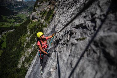 Ferrata üzerinden İsviçre Alplerinde kayaya tırmanan güzel bir bayan tırmanıcı.