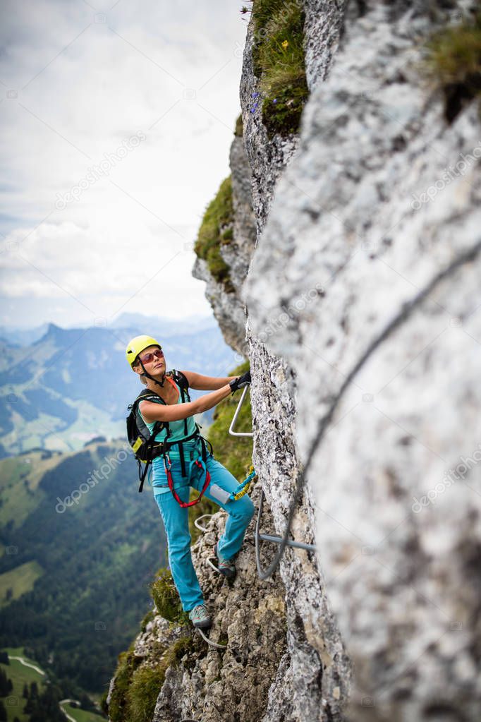 Pretty, female climber on a via ferrata -  climbing on a rock in Swiss Alps