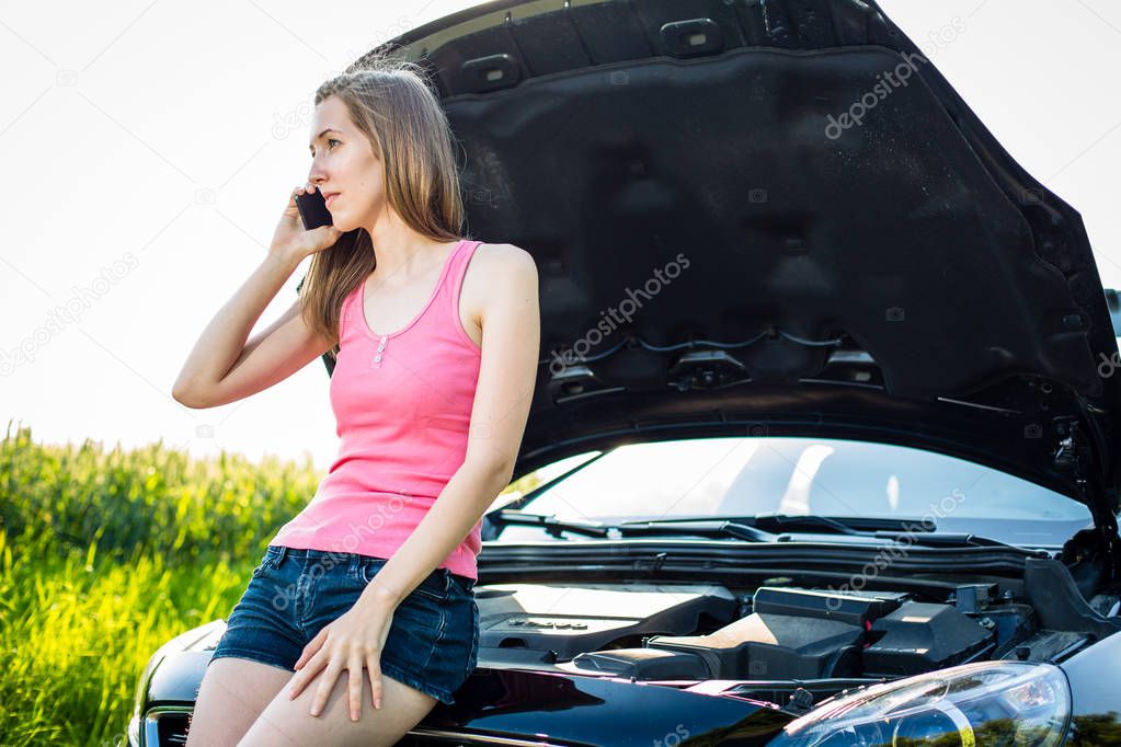 Pretty, young woman by the roadside after her car has broken down