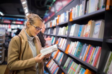 Güzel, genç bir bayan kitapçıdan almak için iyi bir kitap seçiyor.