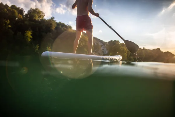 一个英俊的小伙子在桨板上 在温暖的黄昏阳光下 在一条可爱的河上做一个伟大的运动 — 图库照片