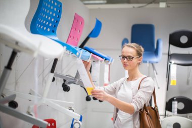 Güzel, genç bir kadın modern bir ev mobilyası mağazasında dairesi için doğru mobilyayı seçiyor (renk tonlu görüntü; sığ DOF)