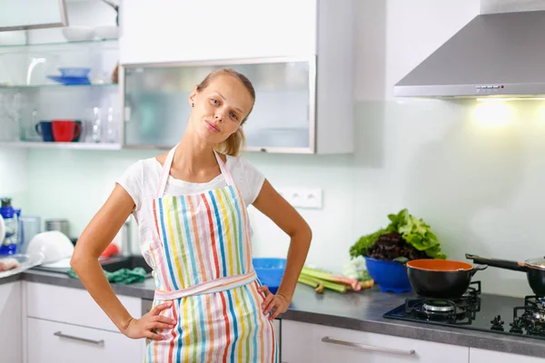 Portrait of a young woman wearing an apron, standing with a confident attitude in her modern kitchen (color toned image; shallow DOF)