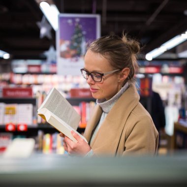 Güzel, genç bir bayan kitapçıdan almak için iyi bir kitap seçiyor.