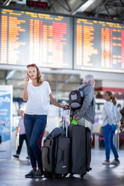 Uluslararası bir havaalanında bavuluyla genç bir kadın, uçuş öncesi kontrol ve güvenlik kontrolünden geçmeden önce
