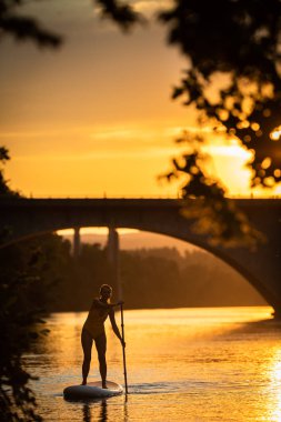 Suyun altından çekilen sıcak öğleden sonra ışığında güzel, genç bir kadın güzel bir gölde kürek çekiyor.