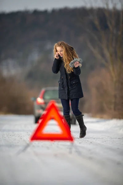 设置一个警告三角形 并呼吁援助后她的车抛锚的中间无处在一个寒冷的冬天日子的年轻女子 — 图库照片