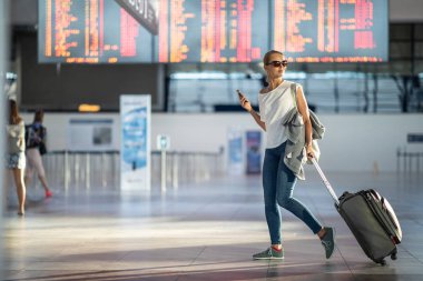 Uluslararası bir havaalanında bavuluyla genç bir kadın, uçuş öncesi kontrol ve güvenlik kontrolünden geçmeden önce