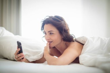 Güzel bir genç kadın güzel bir sabah yatağında cep telefonunu kullanıyor.