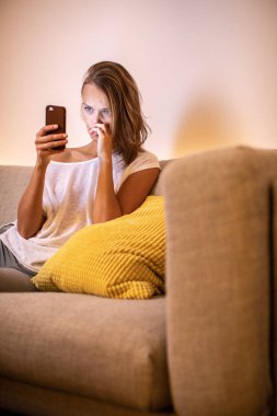 Sevimli genç kadın cep telefonunu kullanarak modern onun evinde rahat bir kanepe