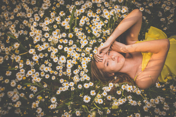 Portrait of young woman with radiant clean skin lying down amid flowers on a lovely meadow on a spring/summer day