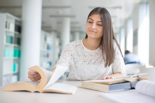 Mooie, jonge college student op zoek naar een boek in de bibliotheek, — Stockfoto
