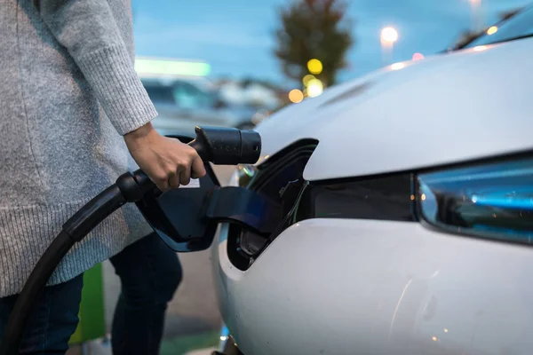 Young woman charging an electric vehicle. Car sharing concept. — Stock Photo, Image