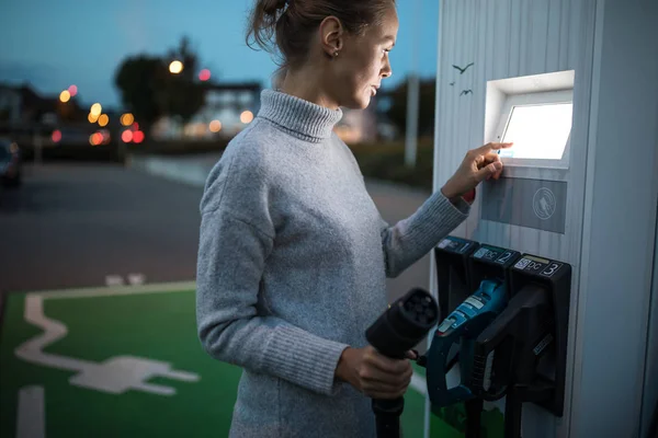 Junge Frau lädt ein Elektrofahrzeug. Carsharing-Konzept. — Stockfoto