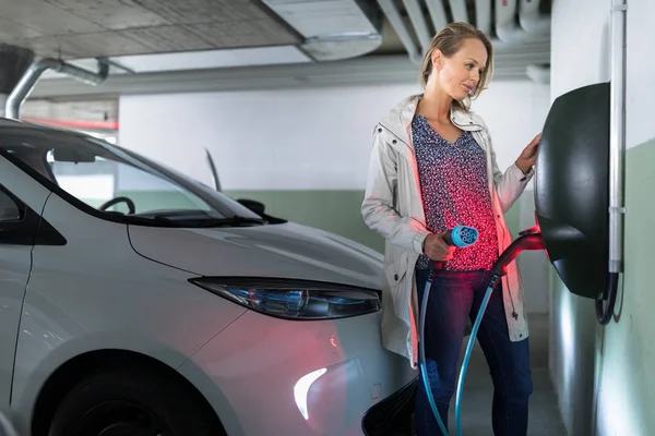 Mujer joven cargando un vehículo eléctrico en un garaje subterráneo — Foto de Stock