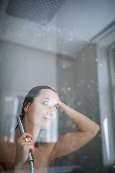 Donna che si fa una lunga doccia calda lavandosi i capelli in un desi moderno — Foto Stock