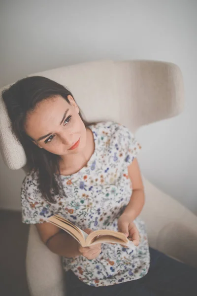 Cute young woman reading a book in a designer chair — Stock Photo, Image