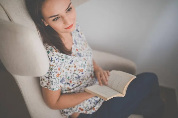 Nette junge Frau liest ein Buch im Designerstuhl — Stockfoto