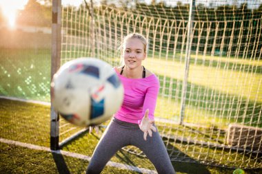 Genç kadın kaleci bir futbol oyunu sırasında bir atış yakalamak